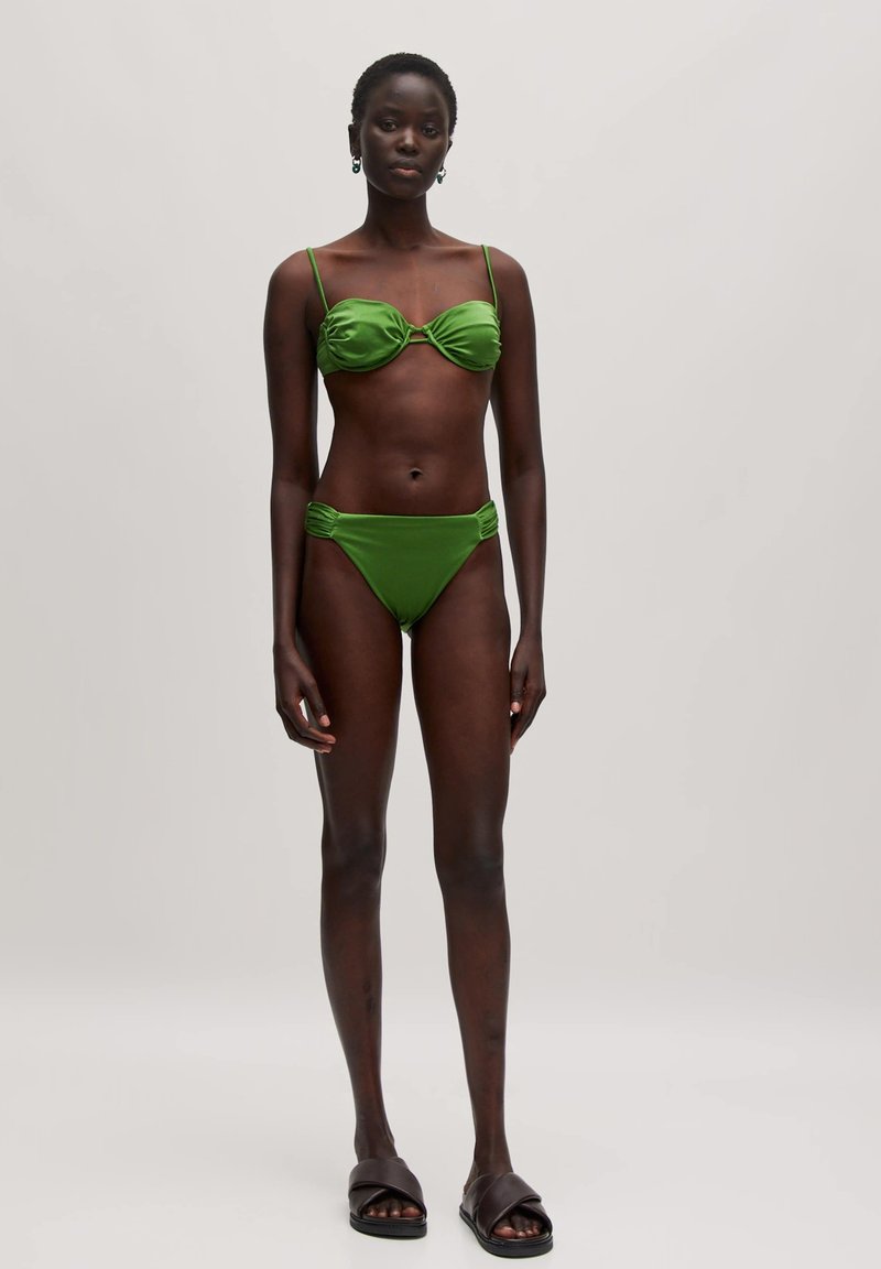 Groene bikini-set met een geraffineerde bandeau-top en high-waisted broekjes met ruching. Gladde textuur, verstelbare bandjes, minimale hardware.