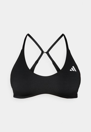 Melns sporta krūšturis ar gludu tekstūru, kam ir racerback dizains un Adidas logotips baltā krāsā. Lences krustojas mugurā.
