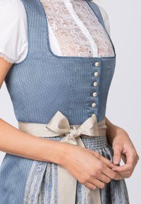 Blauer Dirndl mit strukturiertem Oberteil, Spitzenbluse und beigem Satinband in der Taille. Mit dekorativen Knöpfen und gemustertem Schürze.
