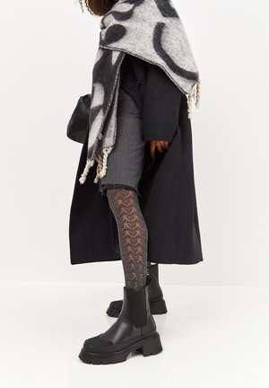 Black ankle boots, gray patterned tights, gray shorts, dark coat, and a large gray and black patterned scarf draped over the shoulder.