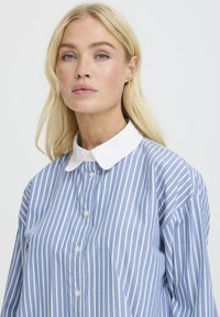 Blauwe en witte gestreepte lange mouw shirt met een witte kraag, met knoopsluiting aan de voorkant en een relaxte pasvorm. Soepele stoftextuur.