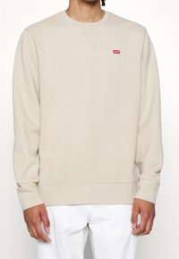 Felpa beige con scollatura rotonda, maniche lunghe, polsini e orlo a coste. Presenta un piccolo logo rosso di Levi's sul petto.