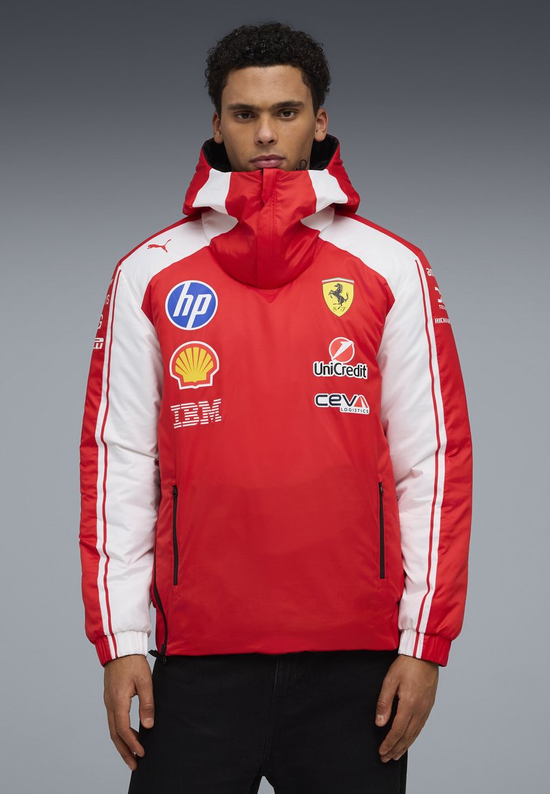 Man wearing a red and white Ferrari racing jacket with sponsor logos including HP, Shell, IBM, UniCredit, and CEVA Logistics.