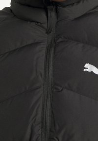 Černá prošívaná bunda s vysokým límcem, plným zipem a malým bílým logem na levé straně. Hladký, lesklý materiál.