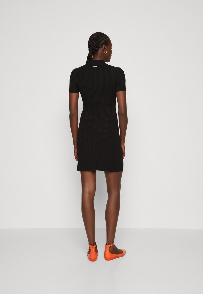 Schwarzes, geripptes Kleid mit kurzen Ärmeln und taillierter Silhouette, zeichnet sich durch einen runden Halsausschnitt und einen Saum über dem Knie aus, kombiniert mit leuchtend orangefarbenen Ballettschuhen.