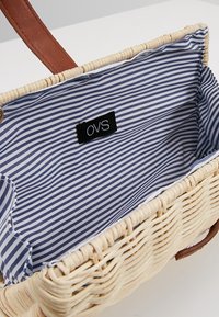 Woven straw bag with brown leather handle. Interior is lined with navy and white striped fabric. Label shows "OVS."