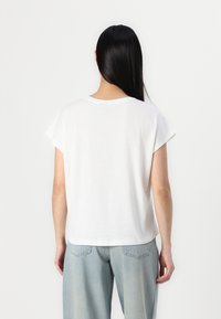 T-shirt bianco a maniche corte in cotone leggero con una vestibilità comoda e un colletto arrotondato, indossato con jeans blu sbiaditi.