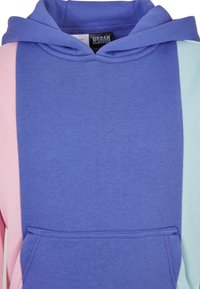 Felpa con cappuccio caratterizzata da un mix di tessuti viola, rosa e azzurro chiaro; texture morbida con tasca frontale e blocchi di colore a contrasto.
