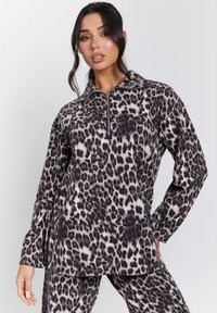 Sudadera de forro polar con estampado de leopardo, con cuello de media cremallera, mangas largas y un ajuste relajado. Textura suave con tonalidades variables de marrón y crema.
