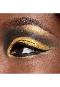Close-up of an eye with gold and black eyeshadow, featuring a bold winged eyeliner and defined lashes, set against smooth skin.