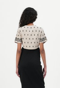 Top corto beige con bordado geométrico negro en las mangas, combinado con una falda negra ajustada. Textura suave, diseño minimalista.