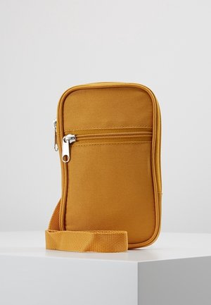 Petit sac bandoulière rectangulaire jaune moutarde avec poche avant zippée et bandoulière réglable assortie sur surface blanche.