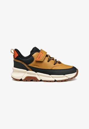 Zapatillas deportivas de exterior en marrón y negro con un upper texturizado, cierre de cordones, correa ajustable y una suela gruesa blanca con acentos naranjas.