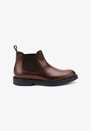 Botín Chelsea de cuero marrón con paneles laterales elásticos y una lengüeta. Presenta una suela de goma negra y un acabado suave.