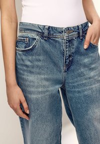 Heled sinise värvusega denim teksad, millel on mugav lõige, nupuga sulgemine, viis taskut ja kergelt kulunud kohad, mis lisavad tekstuuri.