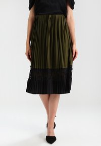 Gonna plissettata con una parte superiore verde oliva e una parte inferiore nera con pizzo. Il materiale ha una texture setosa con un design fluido.