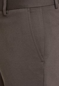 Braune Stretchhosen mit glatter Textur, elastischem Bund und seitlichen Taschen. Sauberes Design mit figurbetonter Silhouette.