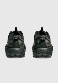 Par de zapatillas de trail running en negro y gris oscuro vistas desde atrás, con suelas rugosas y lados con un patrón de camuflaje.