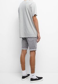 Grijs T-shirt met korte mouwen in combinatie met grijze denimbroekjes, opgerold aan de onderkant, gedragen met witte sokken en zwarte instapschoenen.