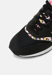 Sneaker noir à l'avant avec embout en mesh, lacets noirs, et accents imprimés léopard rose, jaune et blanc sur la languette et la bordure latérale.
