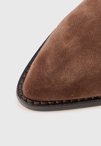 Zapato de ante marrón con un diseño de punta afilada, que presenta una suela cosida en negro para un contraste y una textura suave en la parte superior.