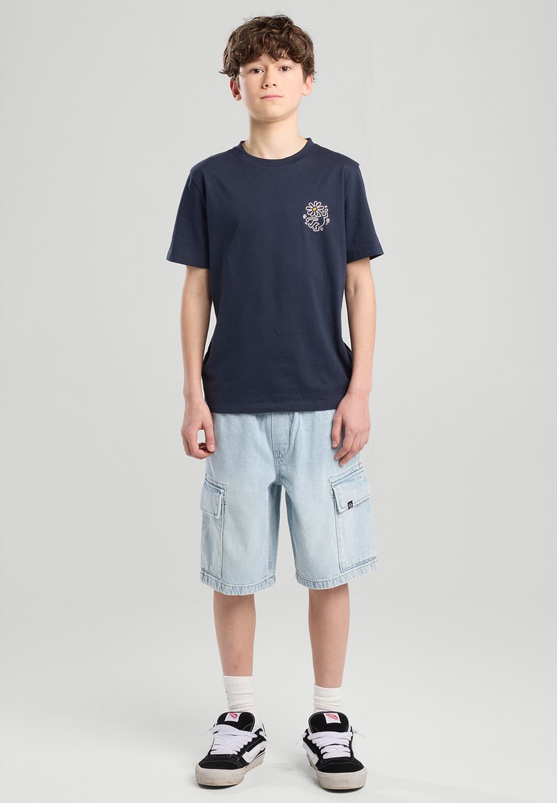 Navy cotton t-shirt with a chest print, paired with light blue cargo shorts featuring side pockets. Black and white sneakers complete the look.