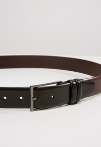 Ceinture en cuir brun avec une finition lisse, dotée d'une boucle en métal argenté, de cinq trous espacés de manière égale, et d'un design classique.
