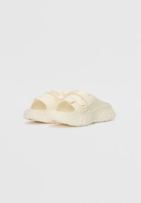 Lys beige glidesandaler laget av gummi med en teksturert såle, justerbar stropp og åpen design. Har logo på stroppen.