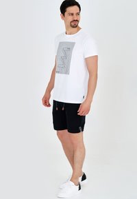 T-shirt blanc avec un motif graphique linéaire noir, associé à un short noir doté de cordons de serrage et de poches latérales. Des baskets blanches complètent l'ensemble.