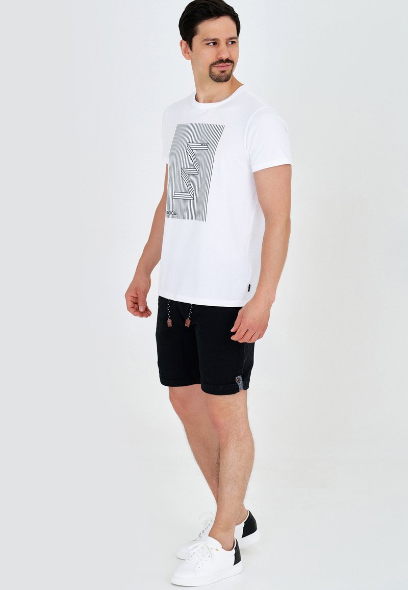 T-shirt blanc avec un motif graphique linéaire noir, associé à un short noir doté de cordons de serrage et de poches latérales. Des baskets blanches complètent l'ensemble.