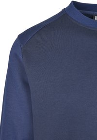 Tumesinine pusa tekstuurse kangaga, ümara kaelusega ja kontrastsete õlapaneelidega. Omad ribaga mansette ja puhta disainiga.