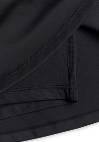 Gros plan de couches de tissu noir montrant un tricot lisse et texturé, avec des coutures et des ourlets visibles.