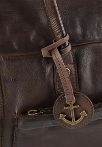 Sac en cuir marron avec une surface texturée, des accessoires en forme d'ancre décoratifs et une sangle en cuir cousue pour la fermeture.