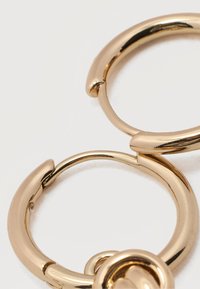 Δύο γυαλιστερά χρυσά σκουλαρίκια κρίκοι με λείο, στρογγυλεμένο σχέδιο σε λευκό φόντο.