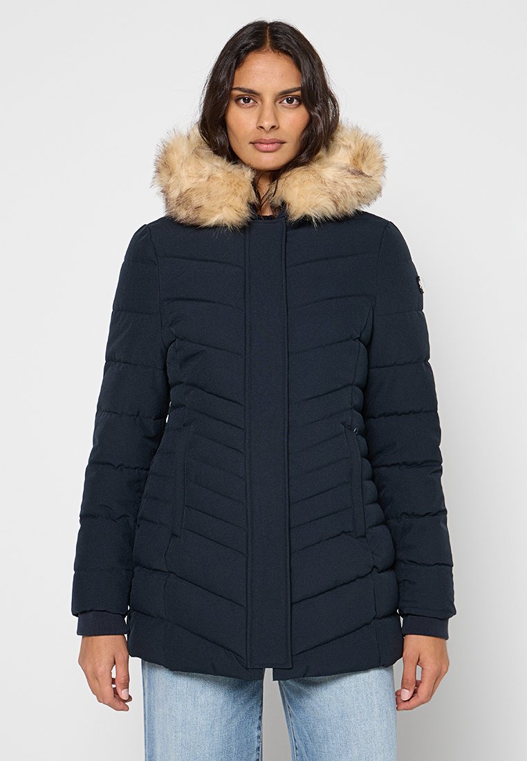 Giacca imbottita blu navy con cappuccio rifinito con pelliccia sintetica, design trapuntato e due tasche laterali. Tessuto liscio con silhouette aderente.