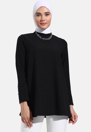 Black long-sleeve tunic with a flared hem, textured fabric, featuring side button details and a silver chain necklace.