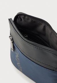 Τσάντα από καμβά σε ναυτικό μπλε με μαύρο δερμάτινο φερμουάρ στην κορυφή. Διαθέτει λεία υφή, γκρι λογότυπο και μια μικρή εσωτερική τσέπη.