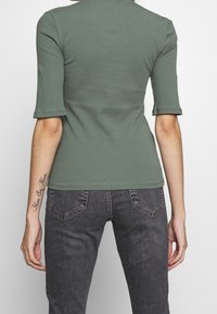 Zelený žebrovaný top s krátkými rukávy, přiléhavý design, kulatý výstřih. Spárován s tmavě šedými džíny s detaily kapes.