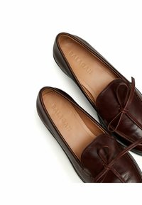 Bruine leren loafers met een gestrikt strikdetail, gladde textuur en een subtiele glans. De binnenkant heeft een geemboste branding. Flexibele zool.