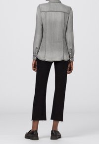 Grey denim shirt with long sleeves and back yoke, paired with black cropped pants featuring frayed hems and sturdy black shoes.