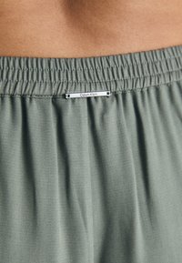 Gröna, lätta tygshorts med elastisk midja, med en liten silverfärgad "Calvin Klein"-etikett på framsidan.