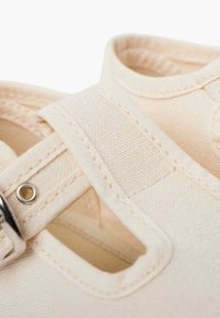 Sandal in tela beige con punta tondeggiante, design a tagli, cinturino regolabile con fibbia metallica e cuciture visibili sulla parte superiore.