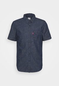 Krátký rukáv košile v tmavě modrém denimu, s klasickým límcem, přední kapsou a knoflíkovým zapínáním. Texturovaná tkanina se šitými detaily.