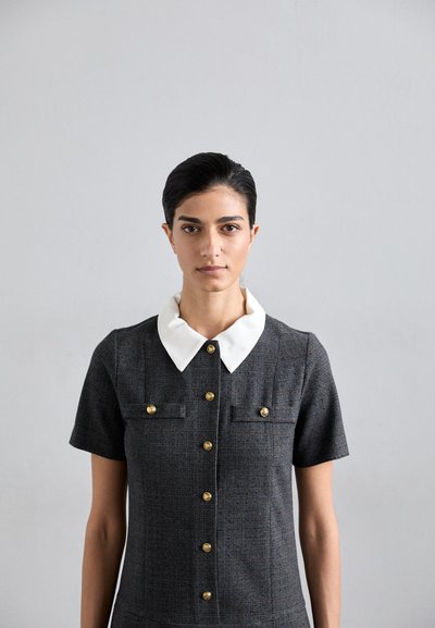 Rochie gri cu mâneci scurte și guler alb, având butoane aurii și două buzunare la piept, confecționată dintr-o țesătură texturată. Design simplu și ajustat.