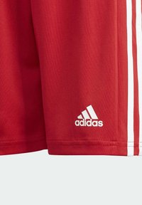Punaiset urheilushortsit, jotka on tehty sileästä kankaasta, joissa on valkoiset pystysuorat raidat ja vasemman alareunan valkoinen kirjailtu Adidas-logo.