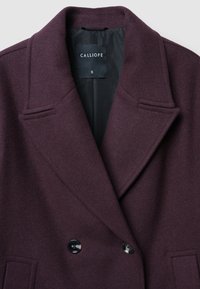 Cappotto in misto lana bordeaux con design doppiopetto, ampi rever a punta, fodera interna nera e due tasche frontali.