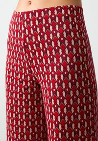Pantaloni rossi con motivo geometrico di diamanti e cerchi in beige e marone, realizzati in un tessuto testurizzato.