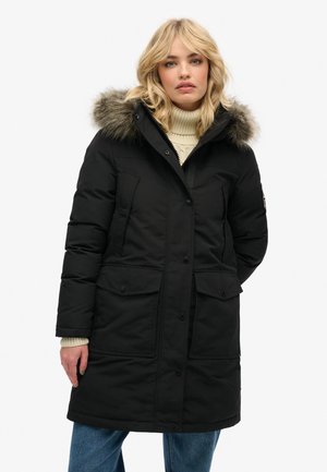 Zwarte gewatteerde parka met een nepbont capuchon, voorkant met drukknoopsluiting, twee grote, met knopen sluitende zakken en een getextureerde gebreide kraag.