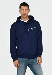Navyblaue Kapuzenjacke aus weichem Stoff mit einer Fronttasche, ausgestattet mit einem weißen Drucklogo und Zugbändern zur Anpassung. Lässiges Design.