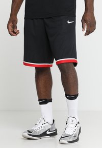 Svarta mesh basketshorts med röd och vit trim, med en liten vit Nike-logotyp på vänster sida. Matchade med svarta och vita skor.